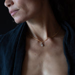 Model wearing a necklace with a hand charm against a dark background