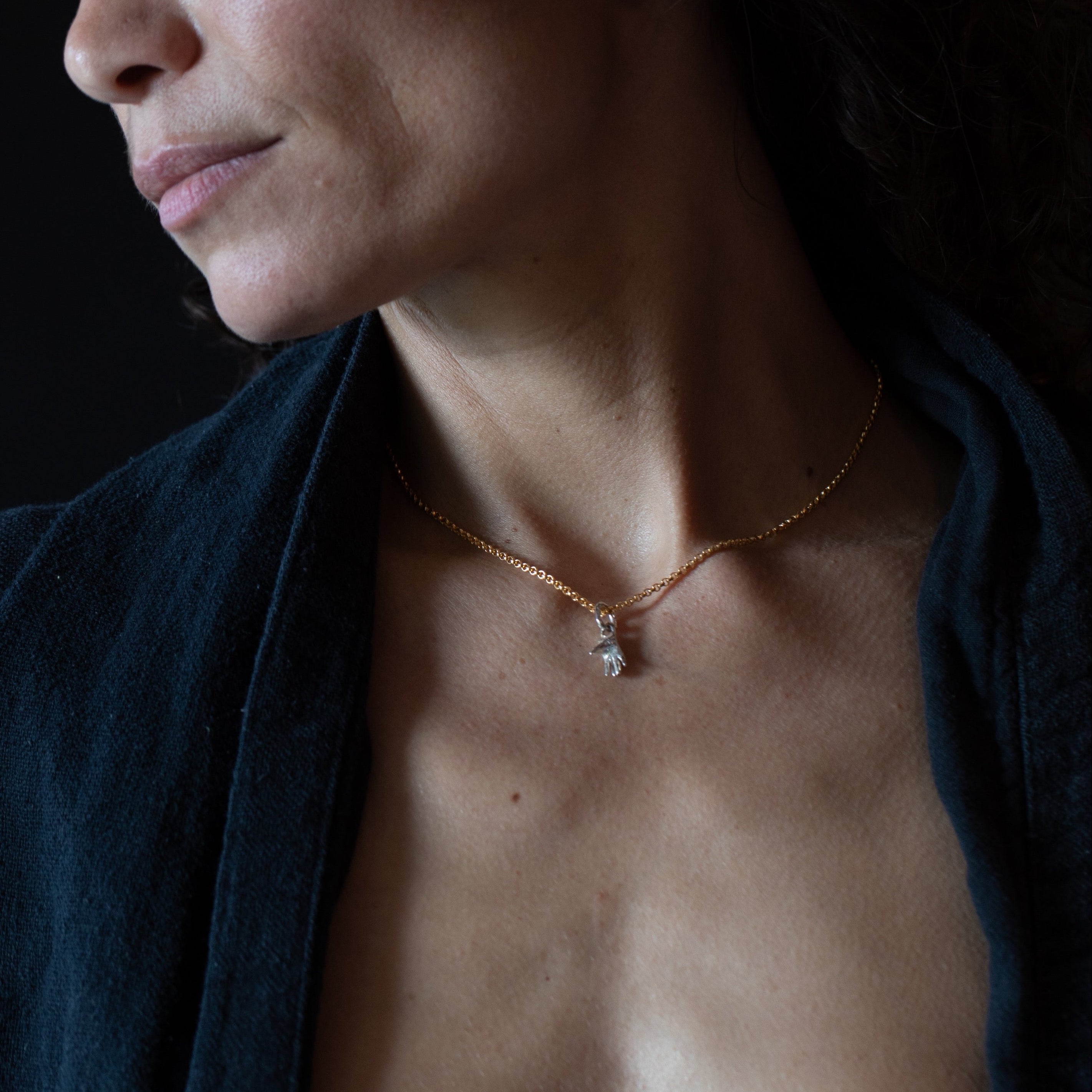 Model wearing a necklace with a hand charm against a dark background