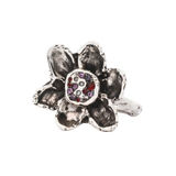 A silver-toned flower ring with textured petals and a central cluster of small gemstones in red, purple, and clear, shown on a plain white background.